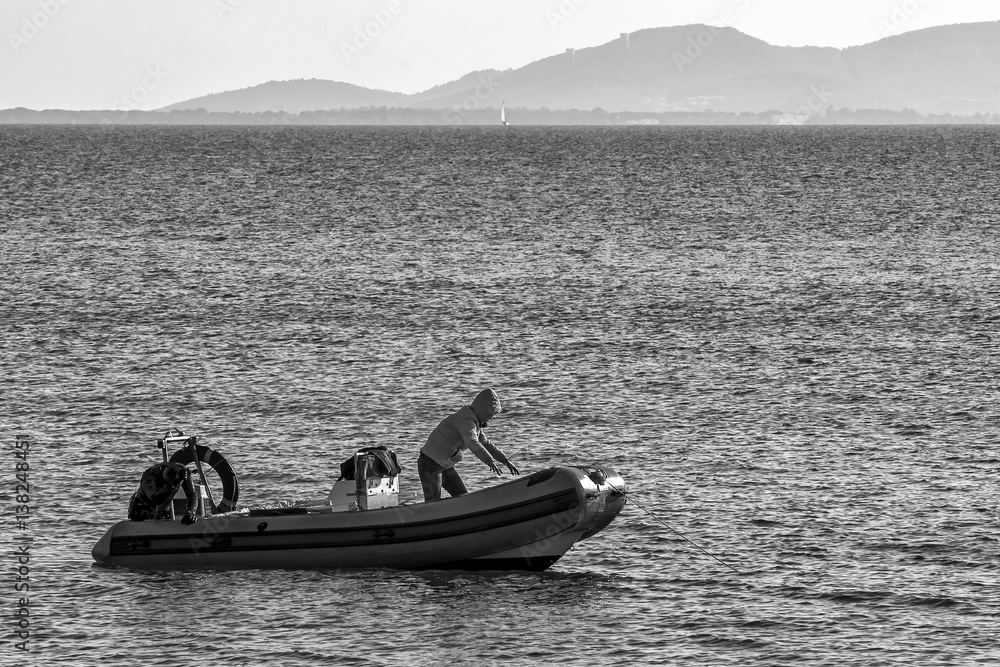Scuba diver on rubber dinghy prepare to dive in water in front of the coast of Talamone, in winter, Grosseto, Tuscany, Italy, in black and white