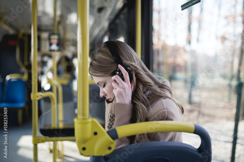 Beautiful young woman sitting in city bus and listening to music.