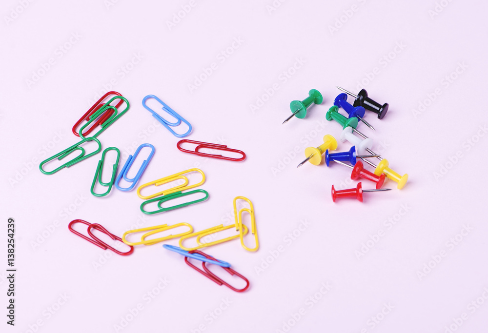 Colorful thumbtacks and clips of two types on pink background.