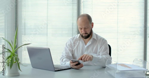 businessman with laptop uses the smartphone in office