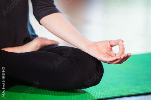 Yoga girl meditating indoor and making a zen symbol with her hand. Closeup of woman body in yoga pose on a green mat