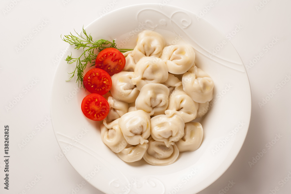Pelmeni with tomatoes and dill. On white plate and white background. Pelmeni with tomatoes and dill. On white plate and white background.