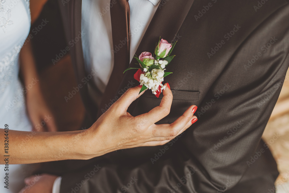 Bride with red manicure corrects boutonniere of small pink roses groom in a suit and tie Bride with red manicure corrects boutonniere of small pink roses groom in a suit and tie
