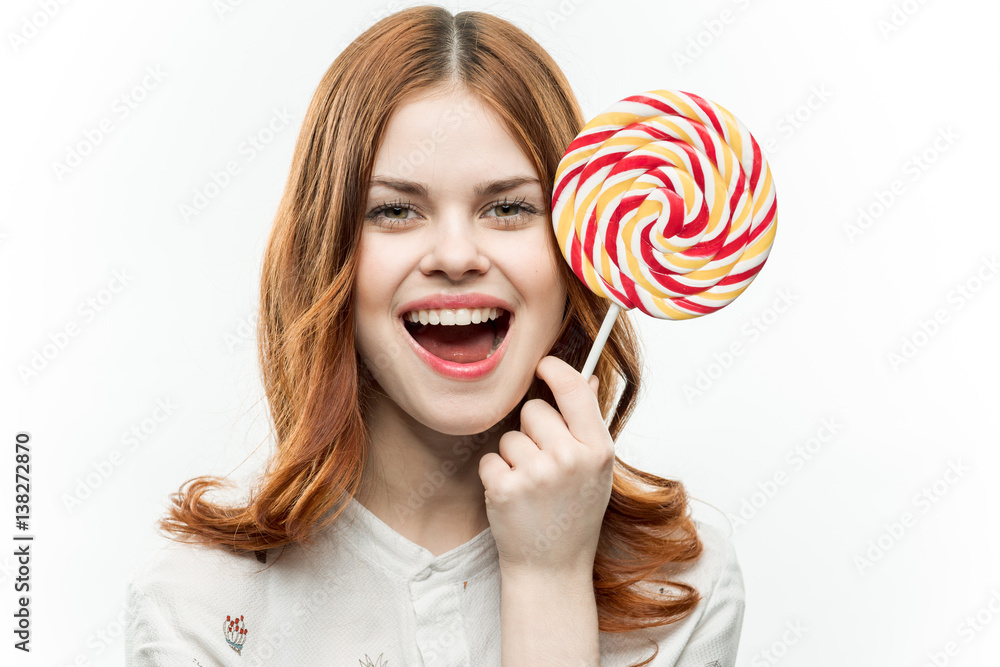 cheerful red-haired woman holding a big candy near the head