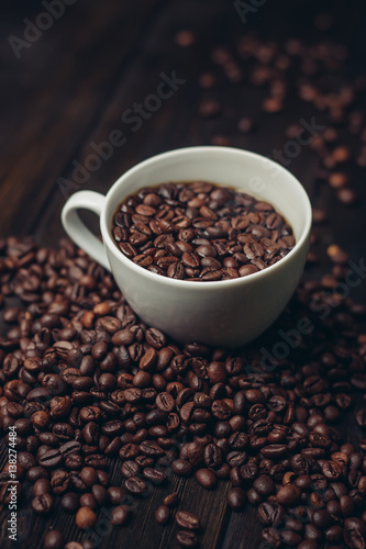 Coffee beans in a white mug and on a wooden table