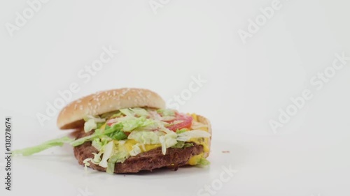 A hamburger falls in slow motion onto a white cyc