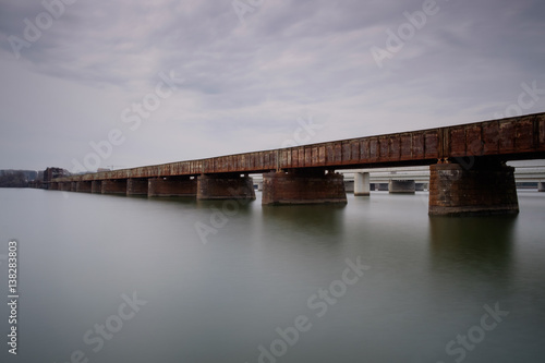 Rusty train bridge over water on a cloudy day