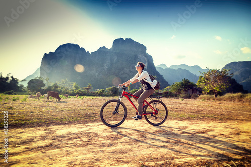 Fototapeta Naklejka Na Ścianę i Meble -  Happy tourist woman riding a bicycle in mountain area in Laos. Travelling in South East Asia
