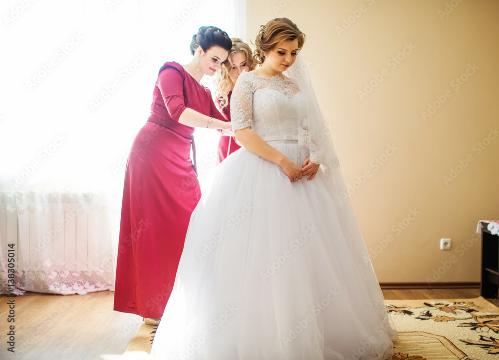 Bridesmaid in red dresses help bride to dressed wedding dress.