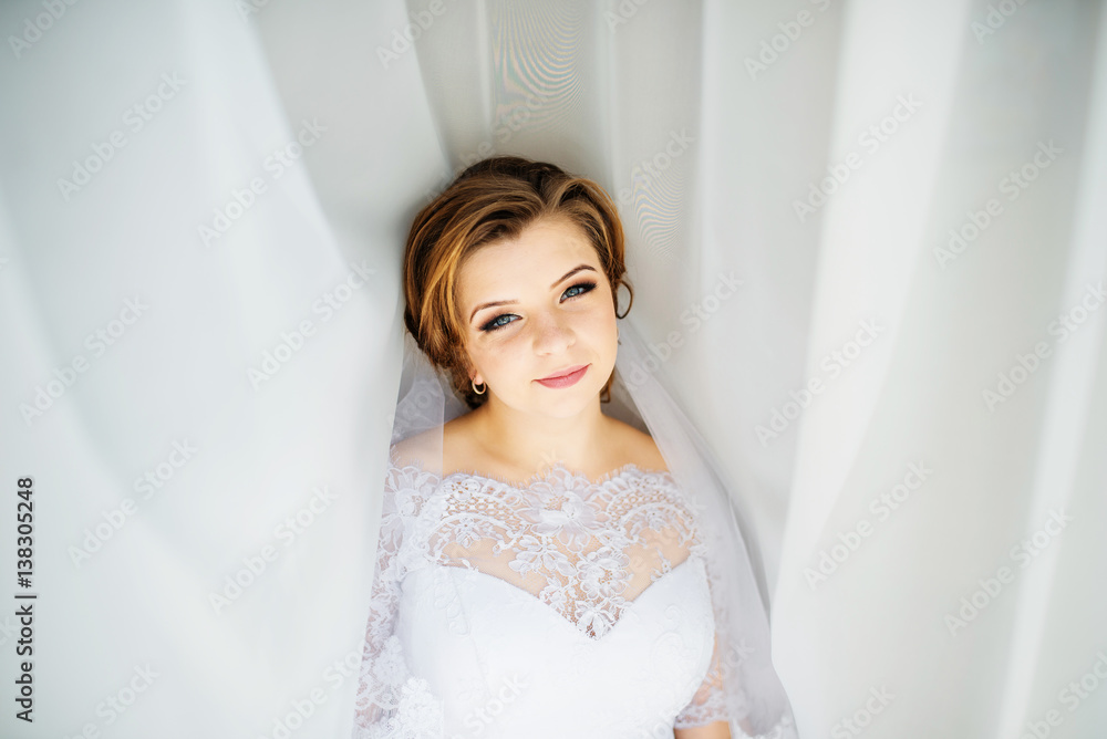 Cute blonde bride posed on curtains at wedding morning day. Cute blonde bride posed on curtains at wedding morning day.