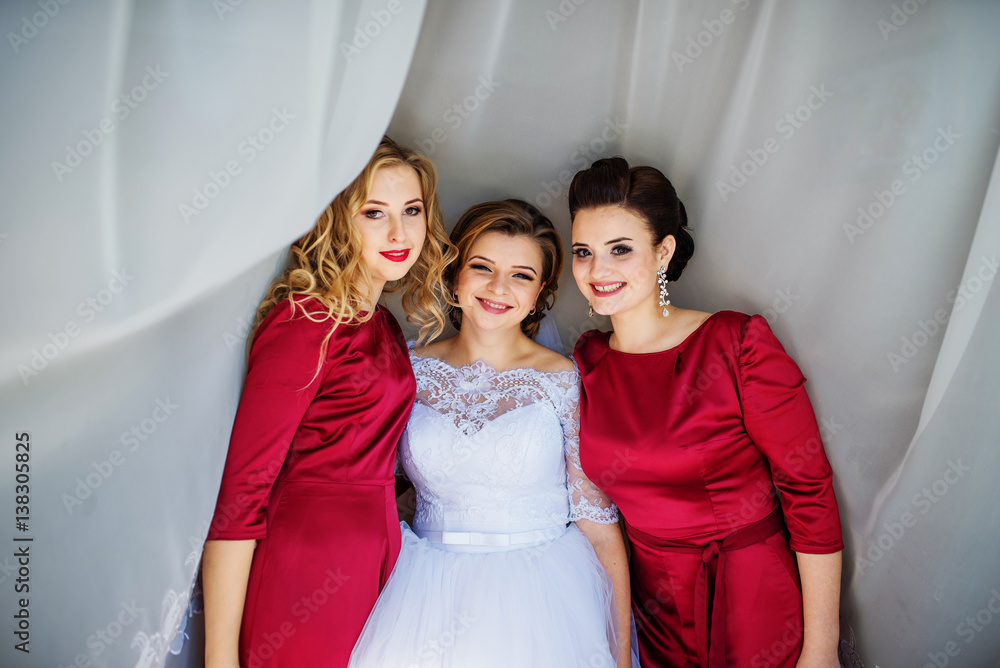 Cute blonde bride with bridesmaids posed on curtains at wedding morning day.