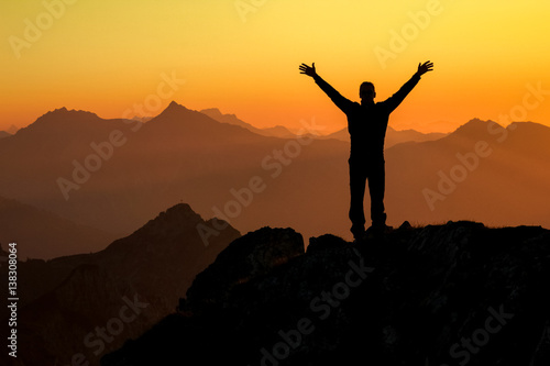 Happy success winning man on summit arms up at sunset