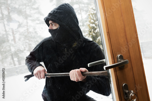 Fotografia house robbery - robber trying open door with crowbar