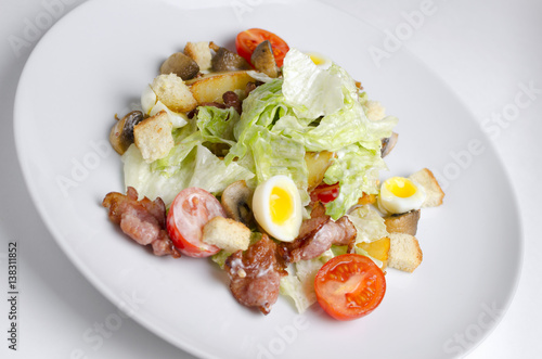 Salad with fried bacon and vegetables on a white plate on a white background