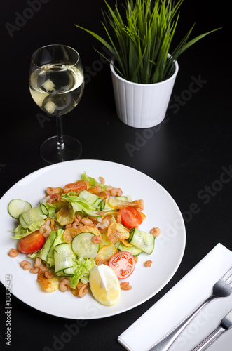 Salad from seafood and vegetables on a white plate on a black table