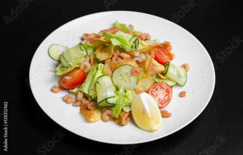 Salad from seafood and vegetables on a white plate on a black table
