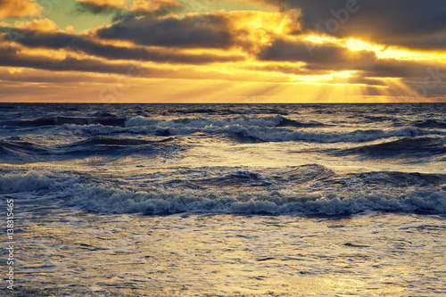 Early morning, sunrise over sea with dramatic cloudy sky. Stormy weather. Waves on the sea. Twilight time.