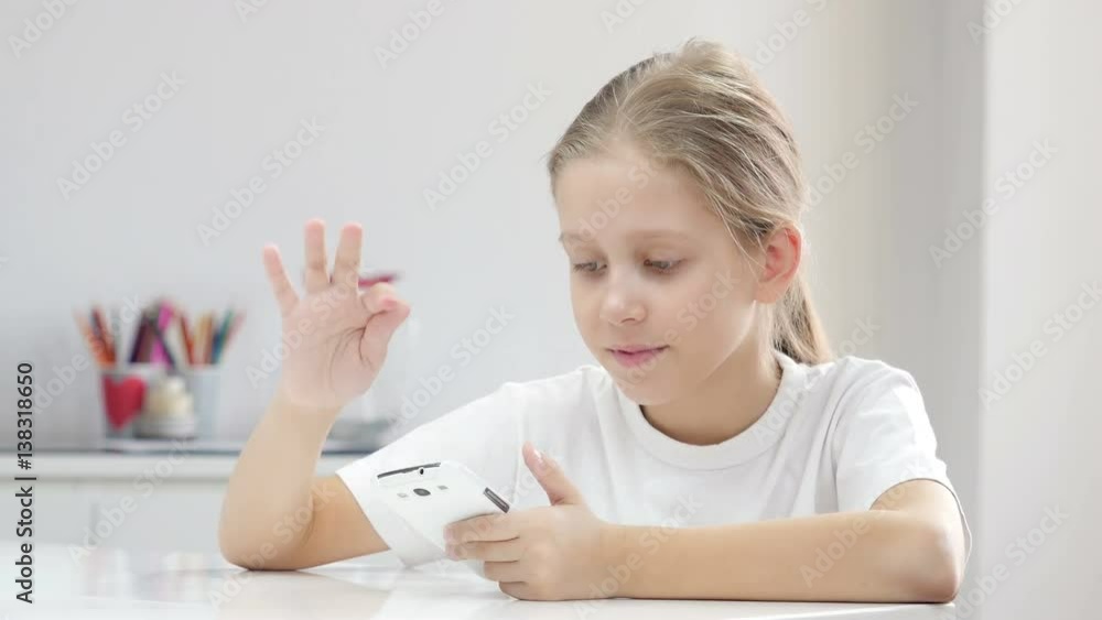Girl sits at the table and uses smartphone, looking at camera and smiling.
Girl sits at the table and uses smartphone, looking at camera and smiling.