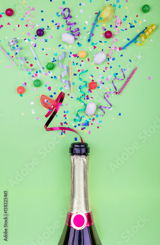 Colorful party attributes fly out from botle of champagne wine. on a GREEN background. Flat lie. Celebrate concept. High resolution photo.