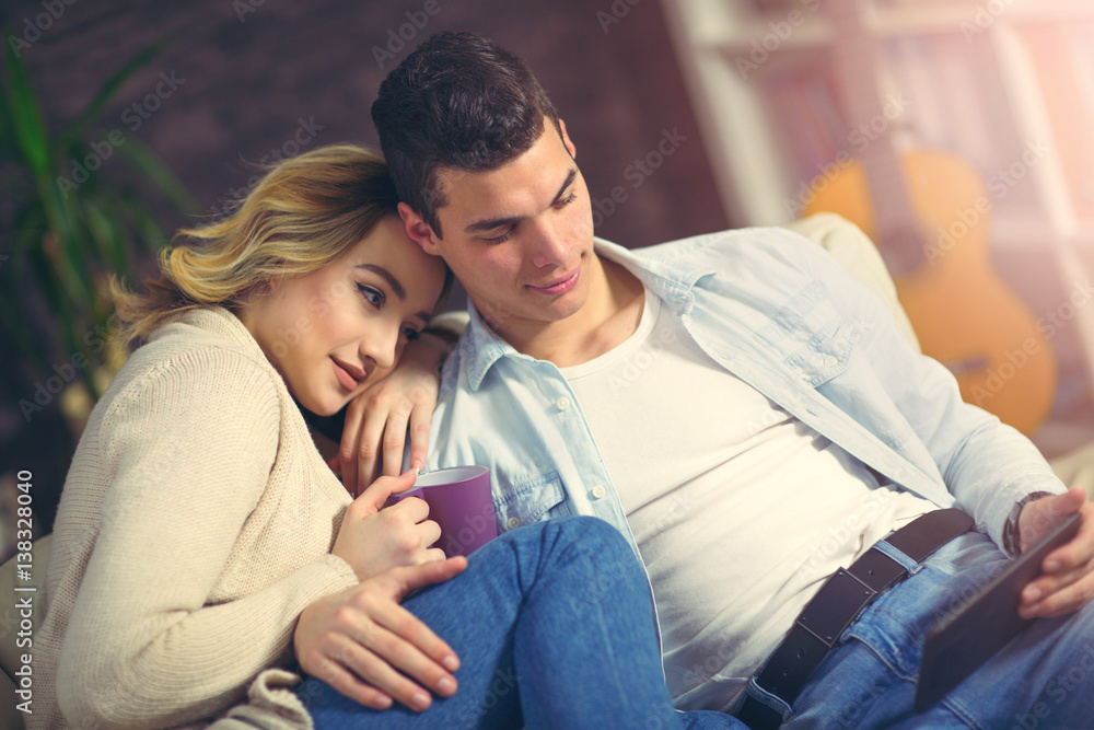 Young couple surfing on the web at home. Smiling woman and man checking mail together on tablet. Happy young couple sitting on sofa and working on digital tablet. Young couple surfing on the web at home. Smiling woman and man checking mail together on tablet. Happy young couple sitting on sofa and working on digital tablet.