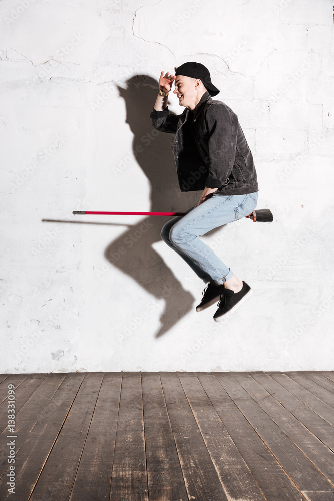 Vertical image of Hipster in snap back flying on mop Vertical image of Hipster in snap back flying on mop