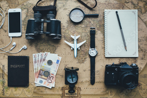 Accessories for travel. Passport, notebook, lens, money, coins, clock, photo camera, smart phone and compass on old vintage map. 