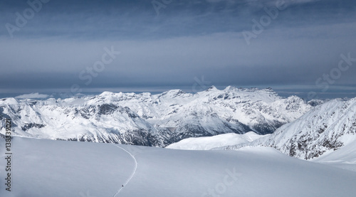 Skier following track leading into valley over untracked snow field