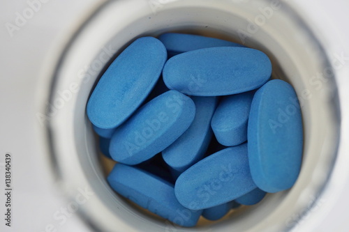Isolated white rounded dose with heap of blue oval pills as a symbol of medicine, healing and pharmacy 