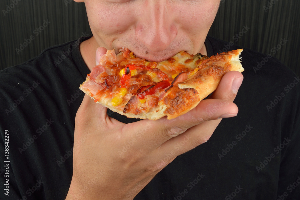 Portrait of a greedy young man eating pizza on a dark background. Fast food, unhealthy