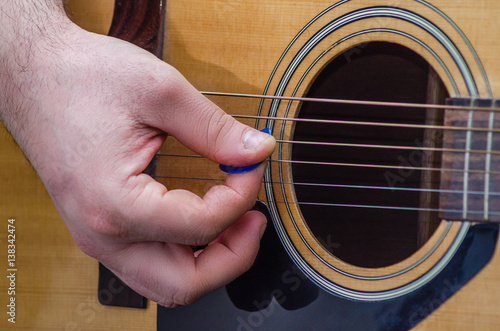 Canvas Print Musician's hand holds a pick on the string of a yellow acoustic guitar