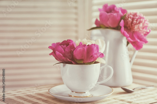 Bouquet of beautiful flowers in cup and vase on table