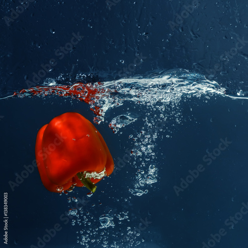 Fresh red bell pepper falling in water on dark background