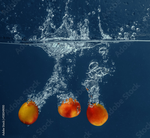 Fresh apricots falling in water on dark background