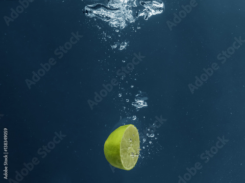 Half of fresh juicy lime falling in water on dark background © Africa Studio