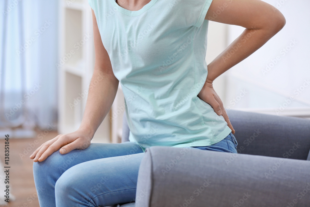 Young woman suffering from backache at home, close up
