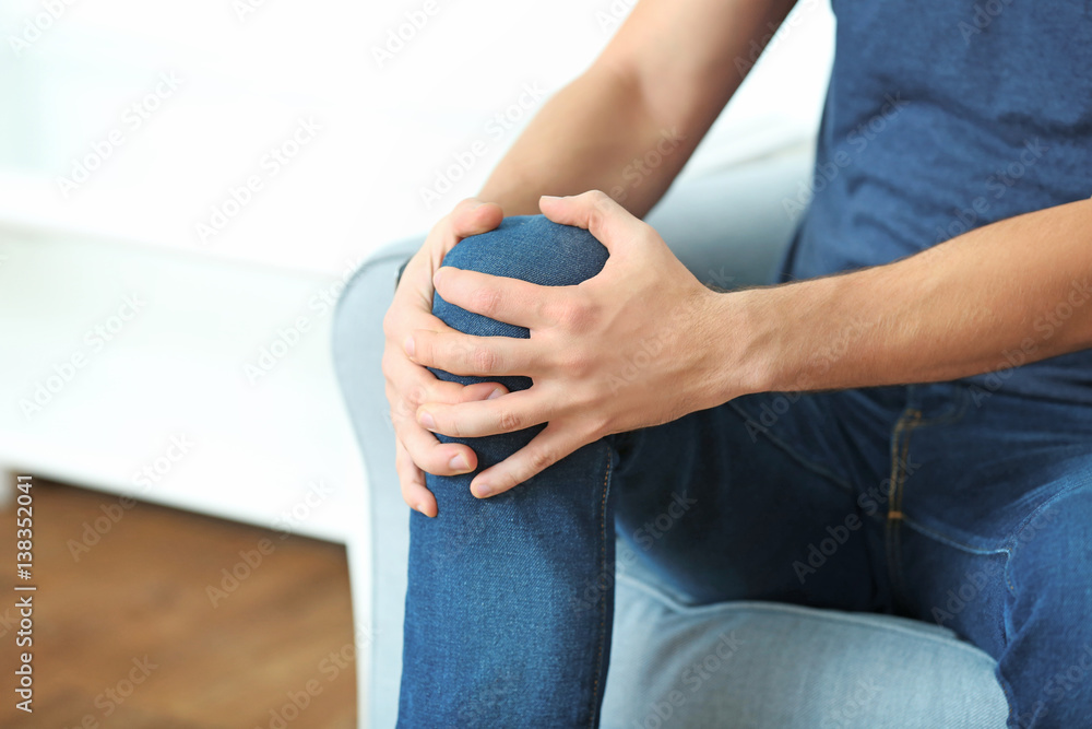 Young man suffering from pain in knee at home, closeup