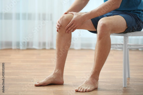 Young man suffering from knee pain at home © Africa Studio