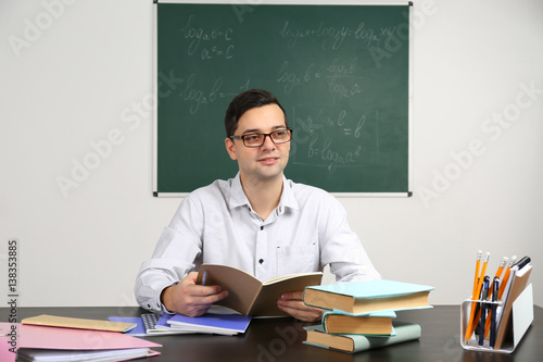 Handsome young teacher sitt...