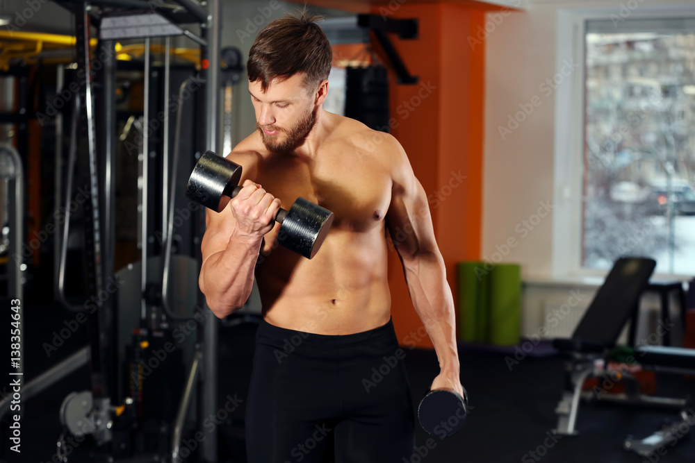Naklejka premium Young handsome man with dumbbells training in gym