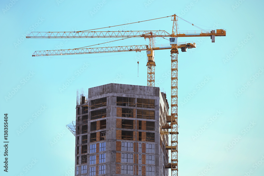 Construction cranes and unfinished building with blue sky on background Construction cranes and unfinished building with blue sky on background