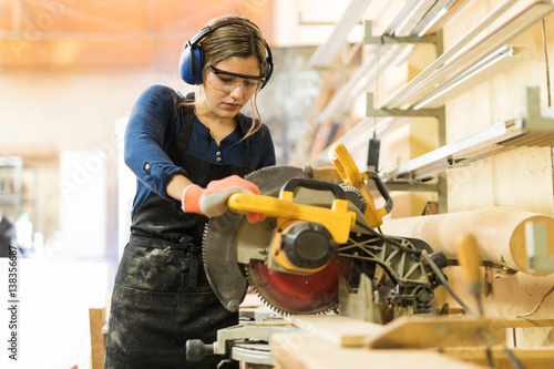 Slika na platnu Woman carpenter using power tools in a wood shop