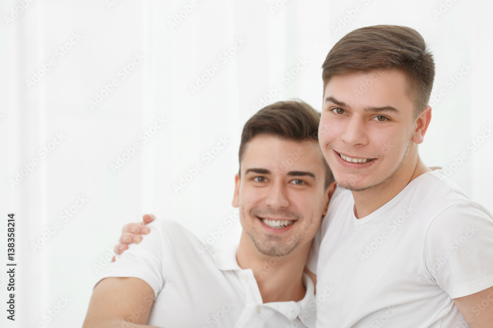 Happy gay couple sitting against window Happy gay couple sitting against window