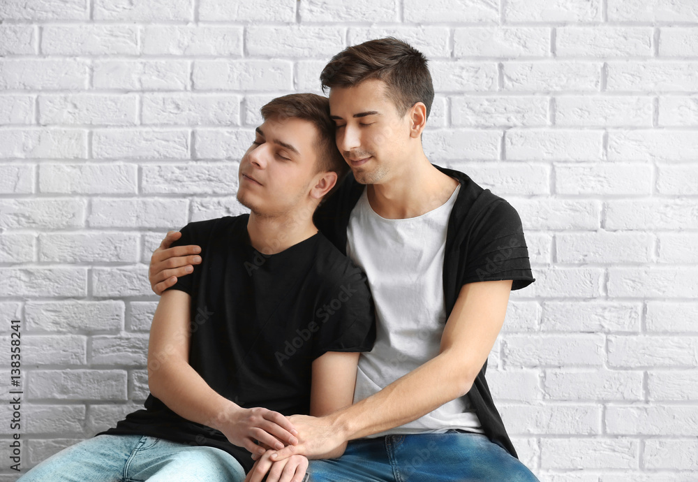 Happy gay couple sitting on white brick wall background
