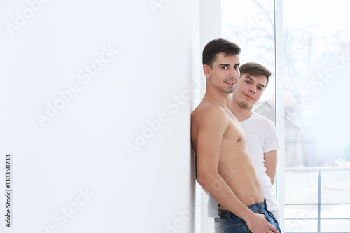 Happy gay couple standing against window