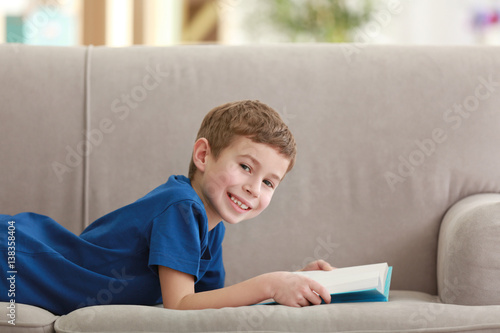 Little boy reading book on sofa indoors