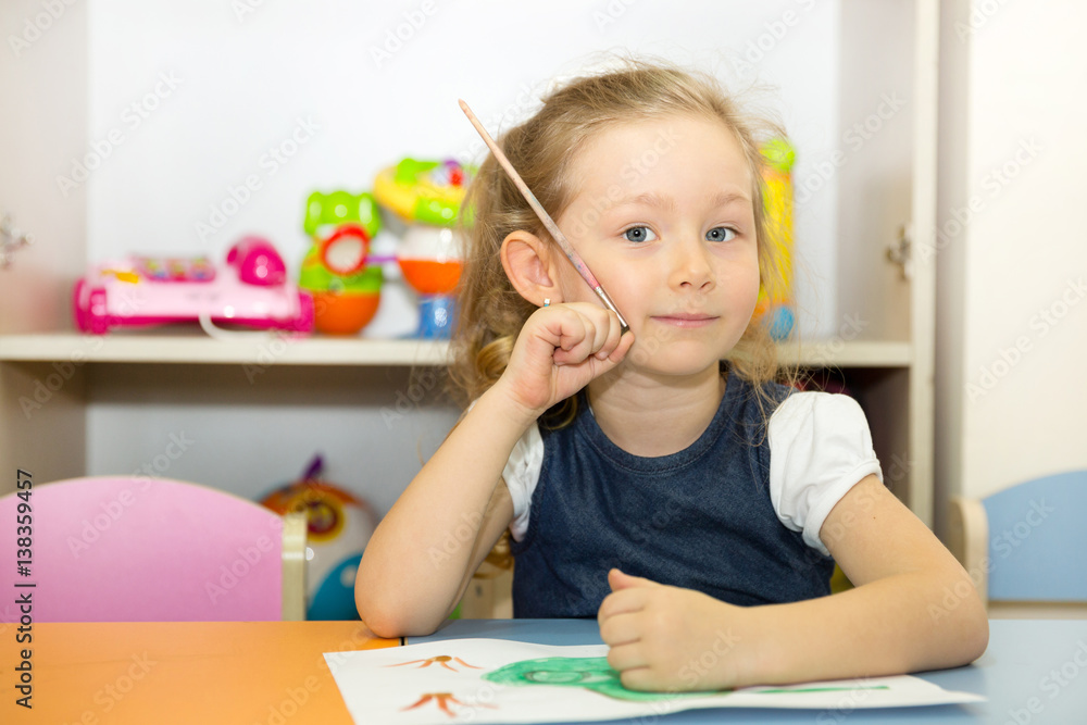 Adorable child girl draws a brush and paints in nursery room. Kid in kindergarten in Montessori preschool class. Adorable child girl draws a brush and paints in nursery room. Kid in kindergarten in Montessori preschool class.