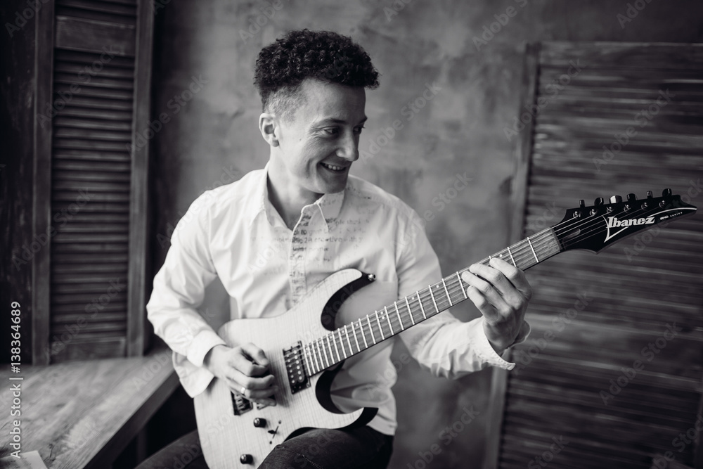 Obraz premium Happy man looks at neck of his electric guitar while he plays on it