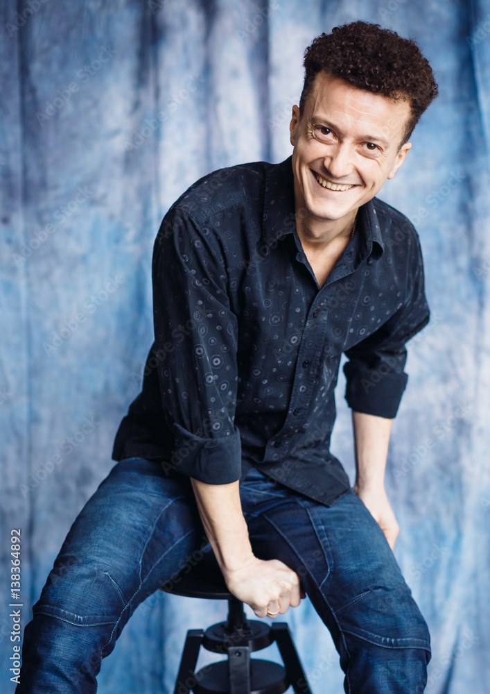 Man in dark blue shirt and jeans sits on black bar chair Man in dark blue shirt and jeans sits on black bar chair