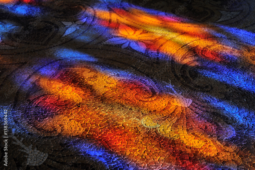 Sunlight through the stained glass window patterns on the stone mosaic floor.