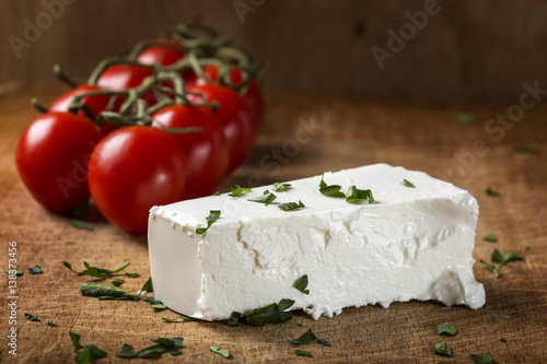 Feta cheese with bunch of cherry tomatoes in background on wood